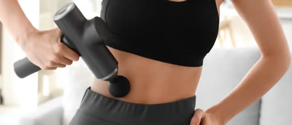 afbeelding van een vrouw die een massage gun op haar buik gebruikt
