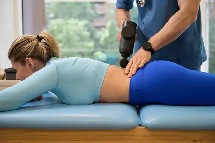 afbeelding van een fysiotherapeut die een massage gun gebruikt